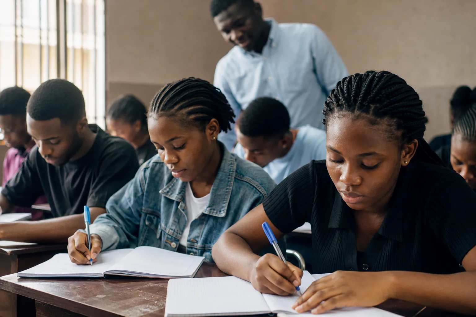 Students writing in a tutorial class while their tutor looks on